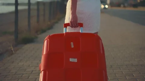 Cinematic close-up of a traveler pulling an orange suitcase on a road Stock Footage 304684741