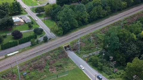 Cinematic drone footage flying over a rural paved road crossing near a railway Stock Footage 344955778