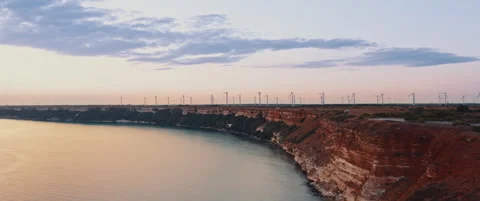 Cinematic flight over a cape at sunset, wind turbines generate energy Stock Footage 247846082