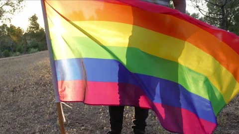 Cinematic footage of non-binary young guy holding a flying rainbow flag Stock Footage 250470832