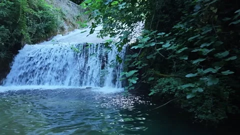 Cinematic low-angle tracking shot revealing a natural waterfall and forest strea Stock Footage 341847632