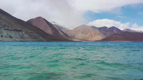 Cinematic low flight over blue water rising to snowy peaks at Pangong Lake .. Stock Footage 336331467