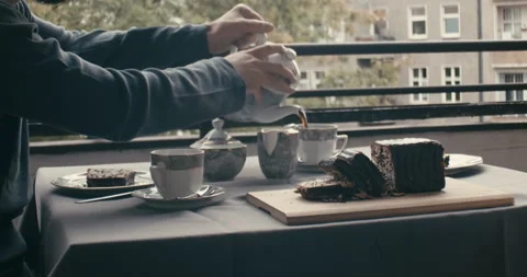 Cinematic medium shot of pouring coffee on set table with cake on balcony Video stock 345922250