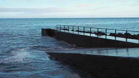 A cinematic ocean scene featuring waves crashing into a concrete pier, sending Stock Footage 346890032