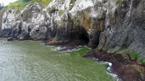 A cinematic reversing drone shot, capturing a sea cave entrance in the side of 库存影片 340931855