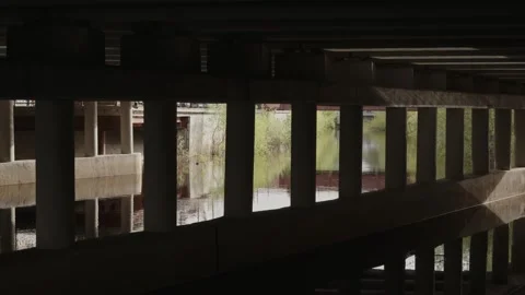 Cinematic shot under concrete bridge pillars reflecting in calm water Stock Footage 335076985