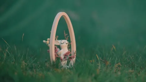 A cinematic shot of a white ceramic Easter bunny figurine nestled in a wooden Видео 331036128