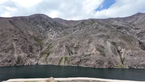 Cinematic Side Road View of a Deep, Dark Green Lake, Framed by Dark Mountain Stock Footage 289193028