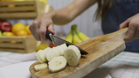 Cinematic slow motion of woman using knife to scrape banana slices off cutting Stock Footage 341196974