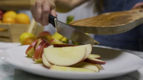 Cinematic slow motion of woman using knife to scrape apple slices off wooden Stock Footage 341214469