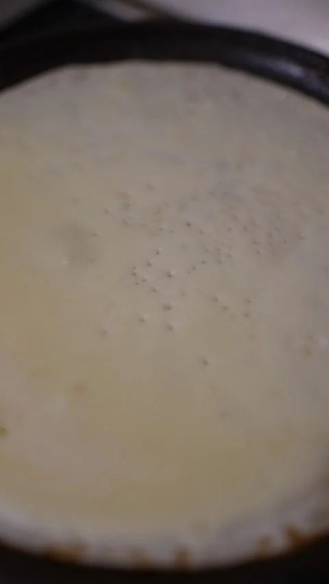 A cinematic, top-down close-up of a thin pancake cooking in a dark frying pan. 库存影片 329318894