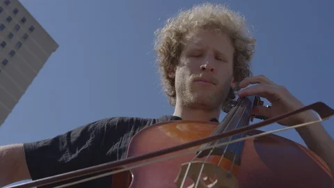 Cinematic upward angle of cellist playing in the sunshine on a summer day Stock Footage 111043254