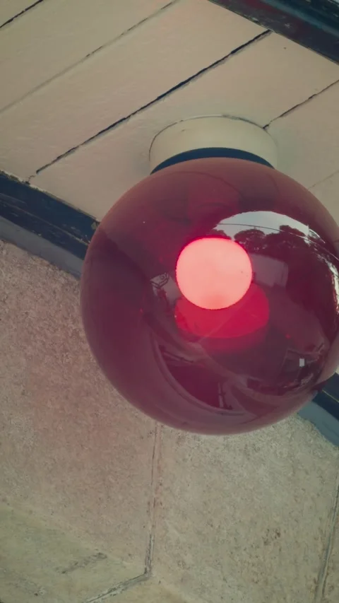 Cinematic vertical close-up shot of a retro red globe ceiling lamp glowing Vidéo 345501018