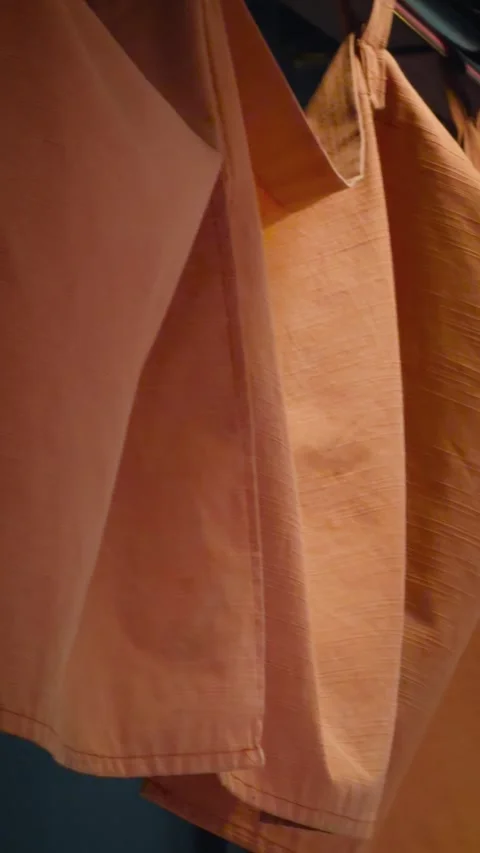Cinematic vertical close-up of textured orange fabric items hanging neatly Vidéo 345514922