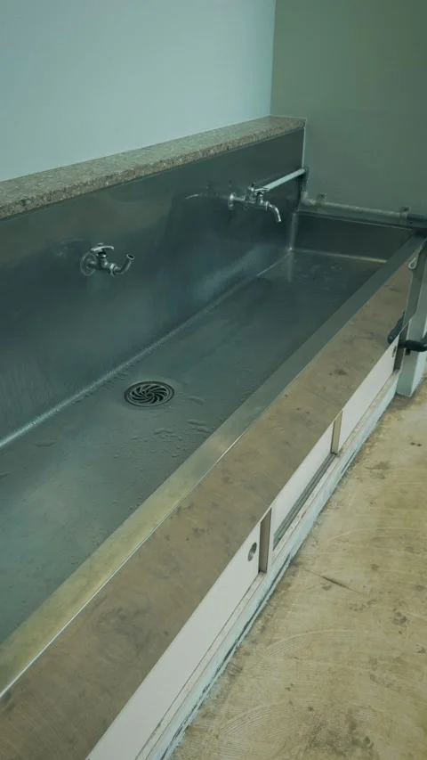 Cinematic vertical shot of an empty wet stainless steel communal sink Vidéo 345458639