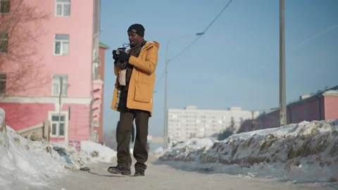 Cinematographer adjusting lens while walking snowy urban walkway 스톡 동영상 318628935