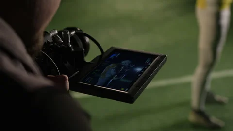 Cinematographer Looking at Viewfinder while Filming Gridiron Football Player Stock Footage 335388846