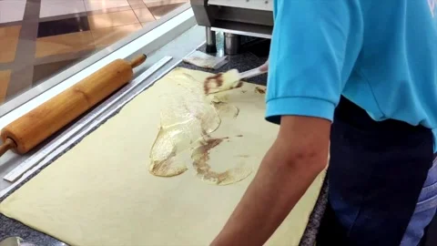 Cinnamon filling being spread on flat dough by worker in blue shirt, focusing on Stock Footage 289236559