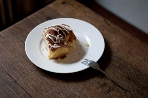 A cinnamon roll on a plate with a bite missing on a table in a coffee shop Stock Photos