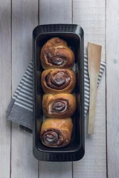 Cinnamon rolls on a black baking pan over a white rustic wooden table Stock Photos