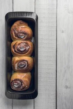 Cinnamon rolls on a black baking pan, over a white rustic wooden table. Stock Photos