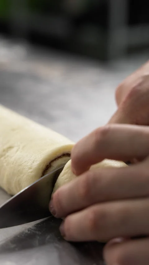 Cinnamon rolls preparation. Pastry chef cuts cinnamon roll using knife Stock Footage 320075004