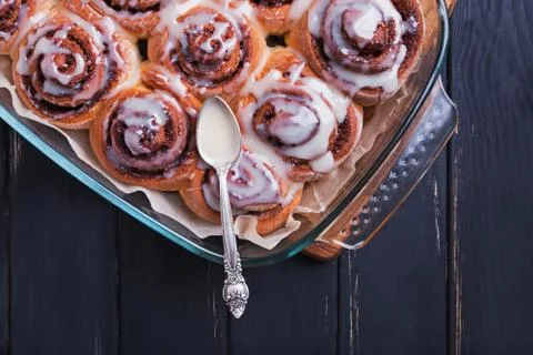 Cinnamon rolls with white icing on top standing on black wooden table Stock Photos