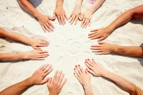 Circle of hands on sand with a sun Stock Photos