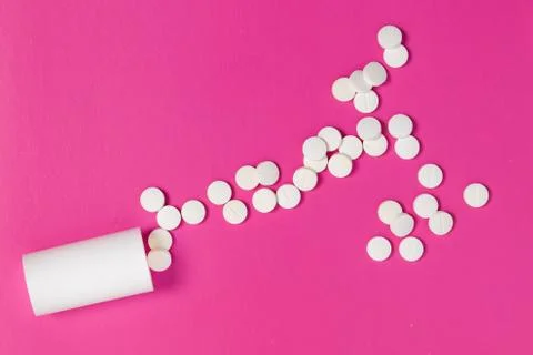 Circle pills tablets spilling out of a white plastic medicine bottle on pink  Stock Photos