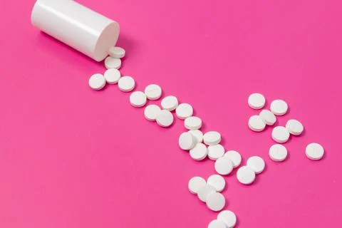 Circle pills tablets spilling out of a white plastic medicine bottle on pink  Stock Photos