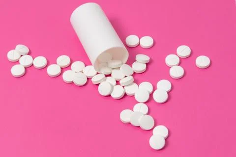 Circle pills tablets spilling out of a white plastic medicine bottle on pink  Stock Photos