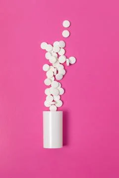 Circle pills tablets spilling out of a white plastic medicine bottle on pink  Stock Photos