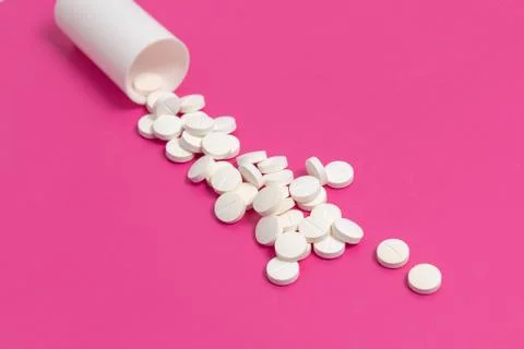 Circle pills tablets spilling out of a white plastic medicine bottle on pink  Foto stock