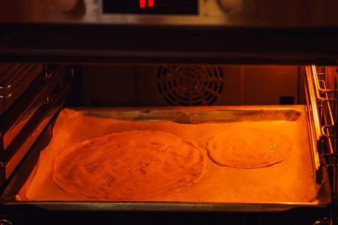 A circle of raw liquid dough on parchment paper is baked in the oven, diet pa Stock Photos
