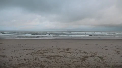Circles of footprints on beach, small waves grey day 動画素材 260503093