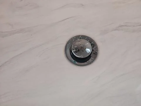 A circular chrome drain installed in a white marble surface, showing modern  Photos