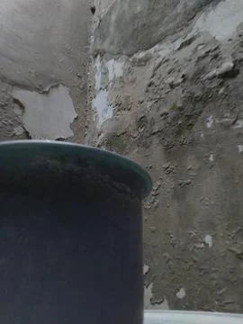A circular dark grey object positioned in front of a weathered grey wall feat Fotos Stock