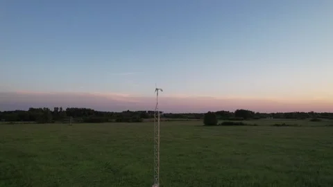 A circular drone fly past a small wind generator on a steel mast during sunset Stock Footage 276113648