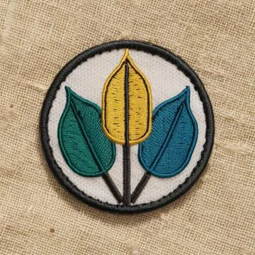 A circular embroidered patch with three stylized leaf shapes in green, yell.. Stock Photos