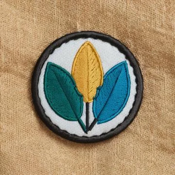 A circular embroidered patch with three stylized leaf shapes in green, yell.. Stock Photos
