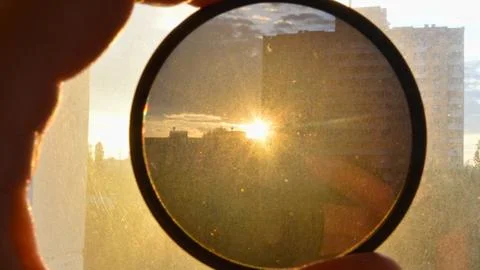 Circular filter held up to a bright sunset sky Stock Photos