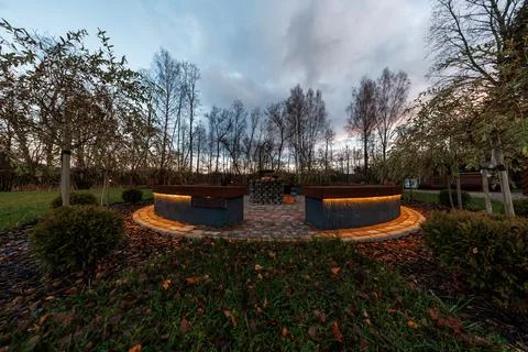 Circular fire pit benches glow at dusk in a late autumn garden 스톡 사진