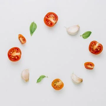 Circular frame made with cherry tomatoes basil garlic cloves white background Stock Photos