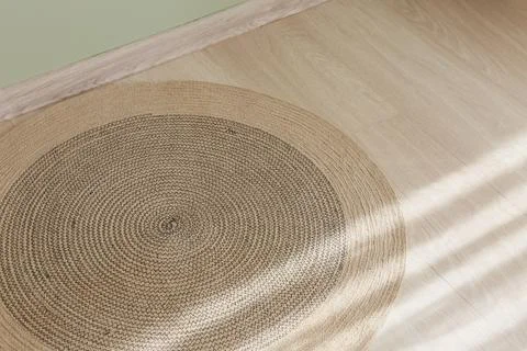 Circular jute area rug on light wood laminate flooring with sunlight shadows, Stock Photos
