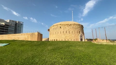 Circular limestone fort tower crowns grassy embankment chain link fence high Видео 343677268