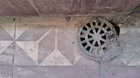 Circular metal drain grate set into weathered geometric stone tiles Stock Photos