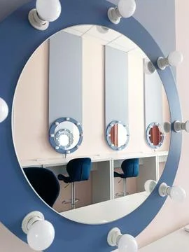 Circular mirror with bright bulbs reflects modern vanity area featuring blue Stock Photos