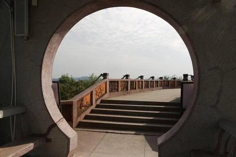 Circular moon gate framing outdoor terrace steps, carved railing, and cloud.. Stock Photos
