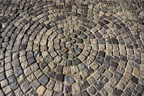 Circular pattern of cobblestone pavement in a public square surrounded by g.. Foto stock