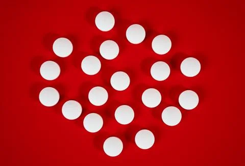 Circular pattern of white tablets on red surface, abstract medical background Foto stock